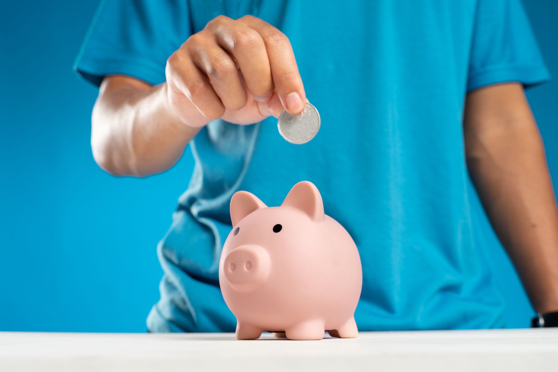 Main déposant une pièce dans une tirelire, symbole de l'épargne et de l'investissement
