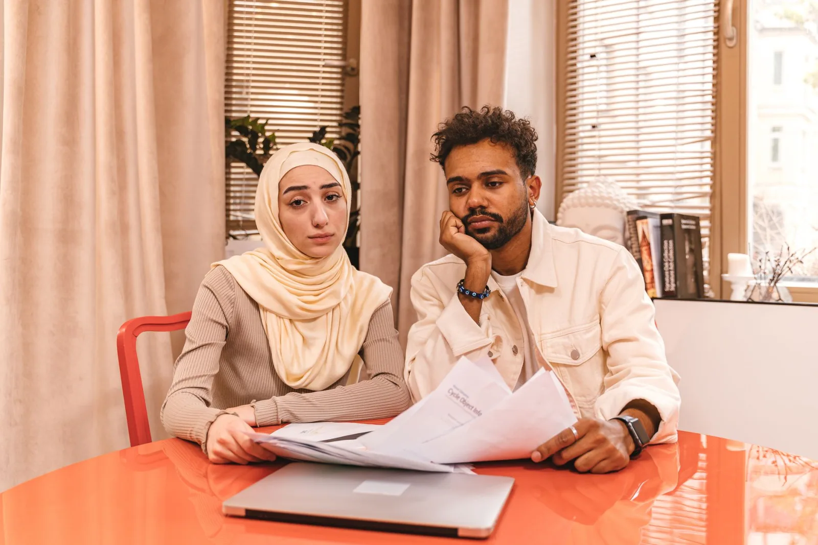 Couple assis à une table examinant des documents financiers devant un ordinateur portable fermé